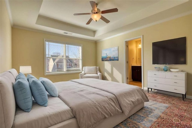 bedroom with a raised ceiling, visible vents, ensuite bathroom, ornamental molding, and baseboards