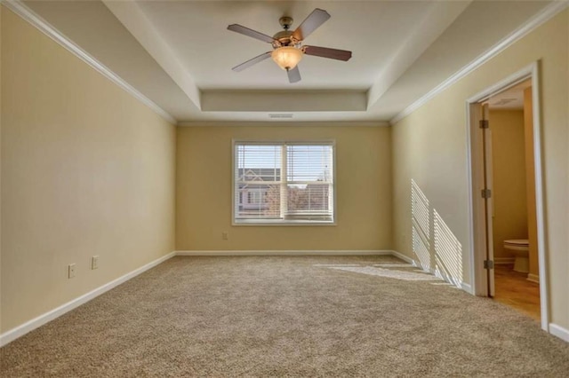 empty room with baseboards, a raised ceiling, ceiling fan, crown molding, and carpet flooring