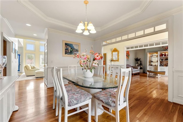 dining room featuring a chandelier, a raised ceiling, wood finished floors, and ornamental molding