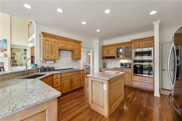 kitchen featuring a center island, stainless steel appliances, glass insert cabinets, a sink, and light stone countertops