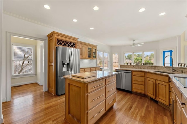 kitchen with stainless steel appliances, a kitchen island, a sink, light wood-style floors, and glass insert cabinets