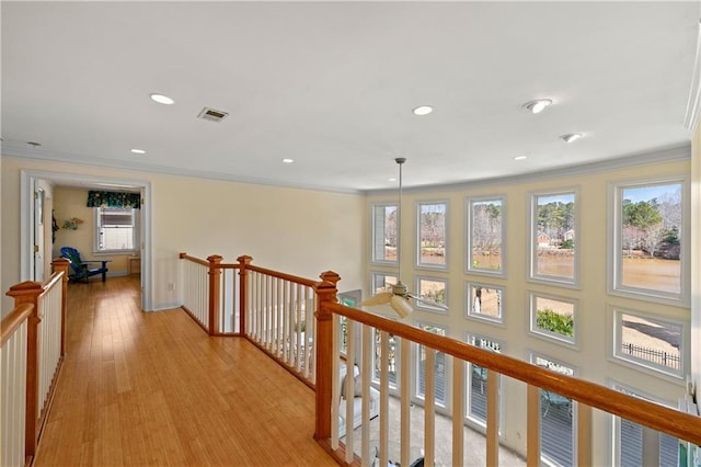 hallway with light wood-style flooring, an upstairs landing, visible vents, and crown molding