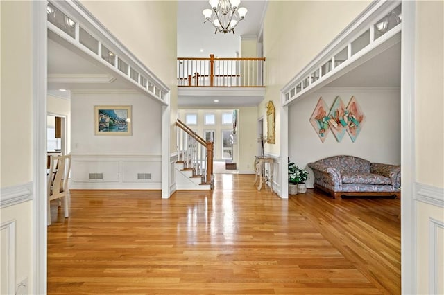 foyer entrance featuring visible vents, stairway, ornamental molding, wood finished floors, and an inviting chandelier