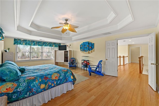 bedroom featuring ceiling fan, a tray ceiling, wood finished floors, and ornamental molding