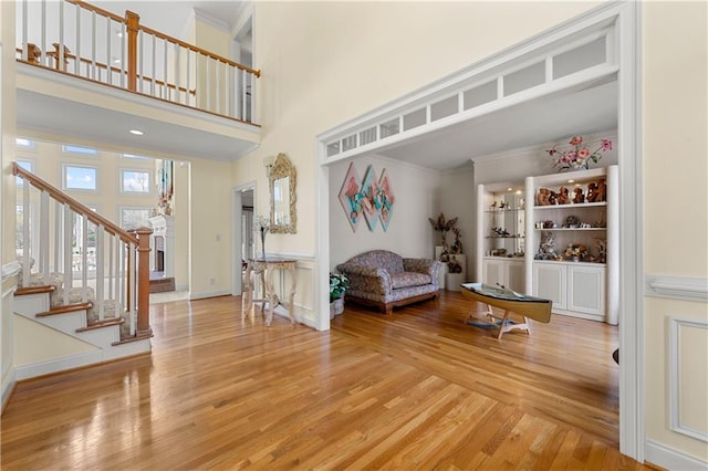 sitting room with light wood-style flooring, crown molding, stairway, and a towering ceiling