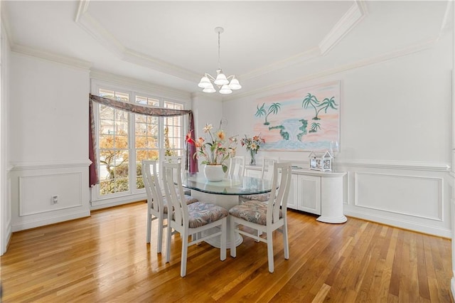 dining area with a chandelier, a tray ceiling, a decorative wall, and light wood finished floors