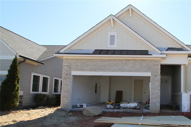 view of front facade with a garage, a shingled roof, stone siding, metal roof, and a standing seam roof