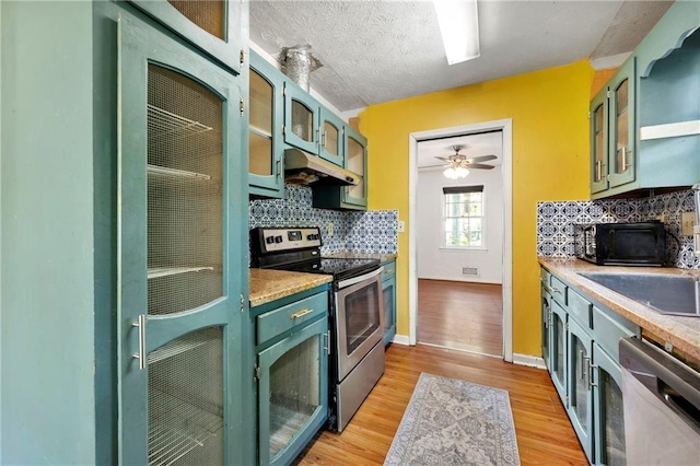kitchen featuring appliances with stainless steel finishes, under cabinet range hood, tasteful backsplash, light wood-type flooring, and glass insert cabinets