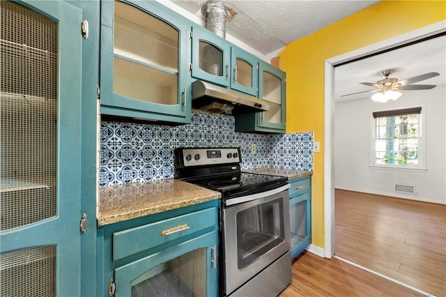 kitchen featuring stainless steel range with electric cooktop, under cabinet range hood, light wood-style floors, decorative backsplash, and a heating unit