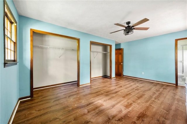 unfurnished bedroom featuring two closets, wood finished floors, and baseboards