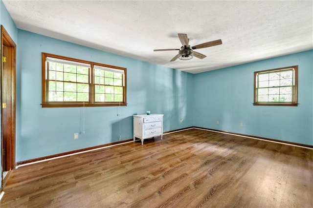 spare room featuring wood finished floors, a textured ceiling, a ceiling fan, and baseboards