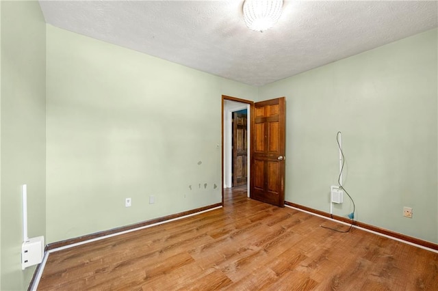 empty room featuring light wood-type flooring, baseboards, and a textured ceiling