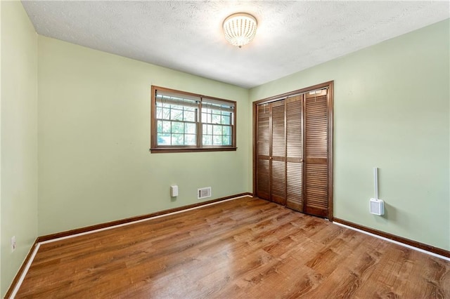 unfurnished bedroom featuring light wood finished floors, a closet, baseboards, and a textured ceiling