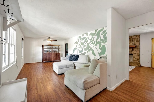 living area featuring wood finished floors, a fireplace, a ceiling fan, and baseboards