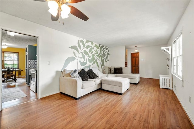 living area featuring light wood-style flooring, a ceiling fan, and baseboards