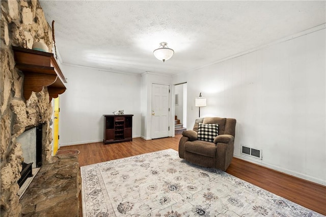 sitting room with a stone fireplace, stairway, wood finished floors, a textured ceiling, and baseboards
