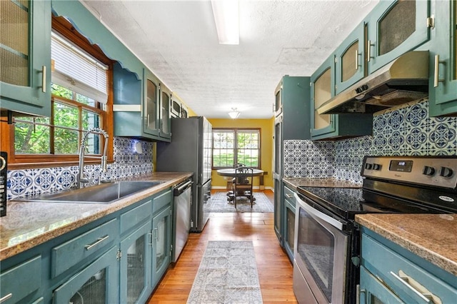 kitchen featuring appliances with stainless steel finishes, green cabinets, under cabinet range hood, a sink, and light wood-style floors