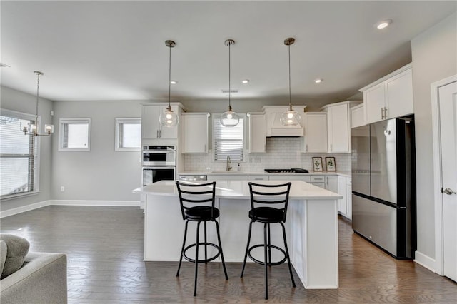 kitchen with appliances with stainless steel finishes, dark hardwood / wood-style flooring, white cabinets, a kitchen island, and hanging light fixtures