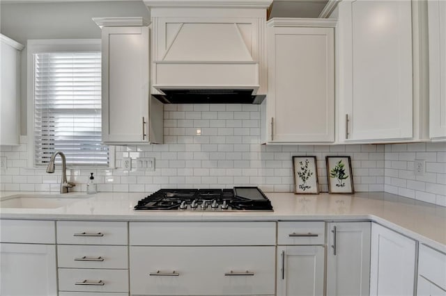 kitchen featuring backsplash, premium range hood, sink, white cabinetry, and stainless steel gas stovetop