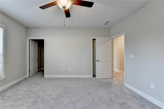 unfurnished bedroom featuring ceiling fan, a spacious closet, and light carpet