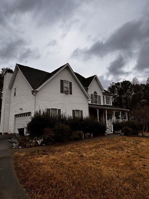 view of front of home featuring aphalt driveway, a chimney, covered porch, and a front lawn