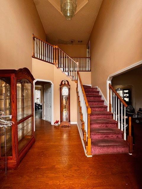 stairway with a high ceiling, wood finished floors, arched walkways, and baseboards