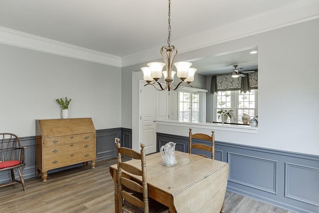 dining space with a decorative wall, crown molding, light wood-style flooring, and a wainscoted wall