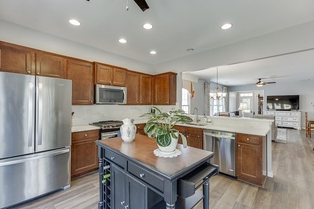 kitchen with a peninsula, ceiling fan with notable chandelier, a sink, stainless steel appliances, and open floor plan