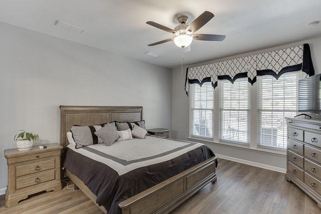 bedroom with baseboards, a ceiling fan, visible vents, and wood finished floors