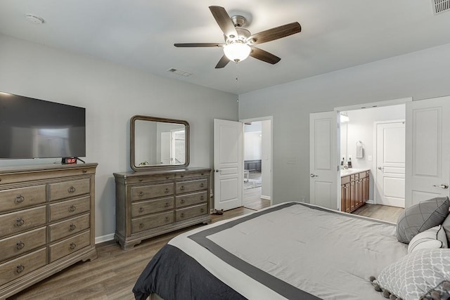 bedroom with connected bathroom, baseboards, visible vents, and wood finished floors