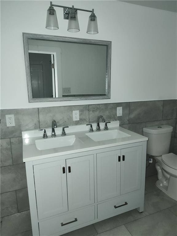 bathroom with toilet, a sink, tile walls, tile patterned floors, and double vanity