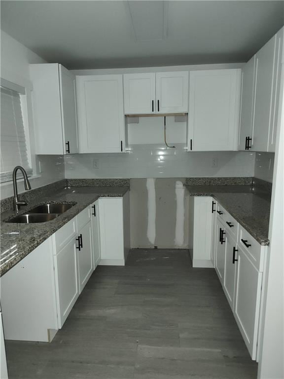 kitchen with dark stone countertops, white cabinetry, and a sink