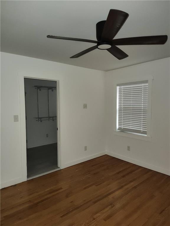 unfurnished bedroom with a closet, a spacious closet, a ceiling fan, wood finished floors, and baseboards