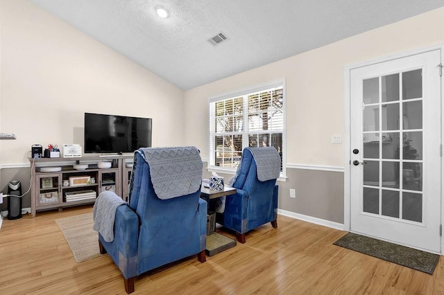 living area with vaulted ceiling, wood finished floors, visible vents, and baseboards