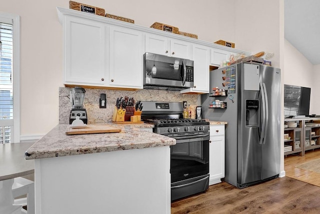 kitchen with light stone counters, stainless steel appliances, decorative backsplash, white cabinetry, and wood finished floors