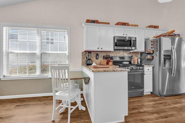 kitchen with light stone counters, stainless steel appliances, wood finished floors, white cabinets, and decorative backsplash