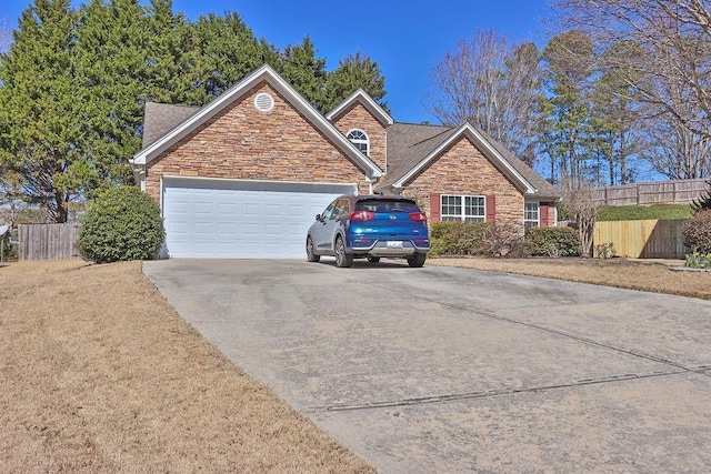 view of front facade with an attached garage, stone siding, fence, and concrete driveway