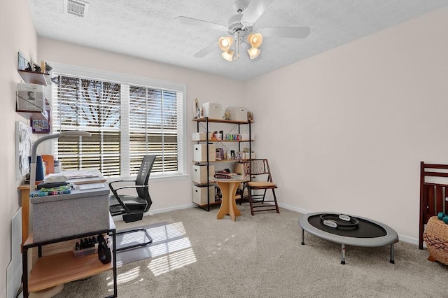 carpeted home office featuring baseboards, visible vents, ceiling fan, and a textured ceiling