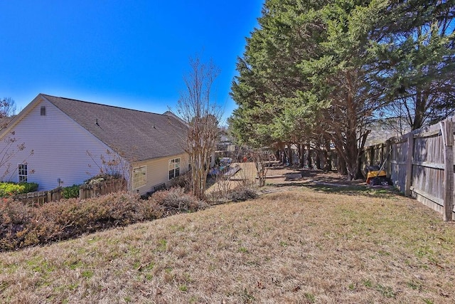 view of side of property featuring a shingled roof, a fenced backyard, and a yard