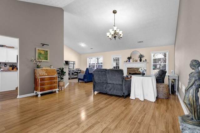 living room featuring a stone fireplace, an inviting chandelier, light wood-style floors, and a healthy amount of sunlight