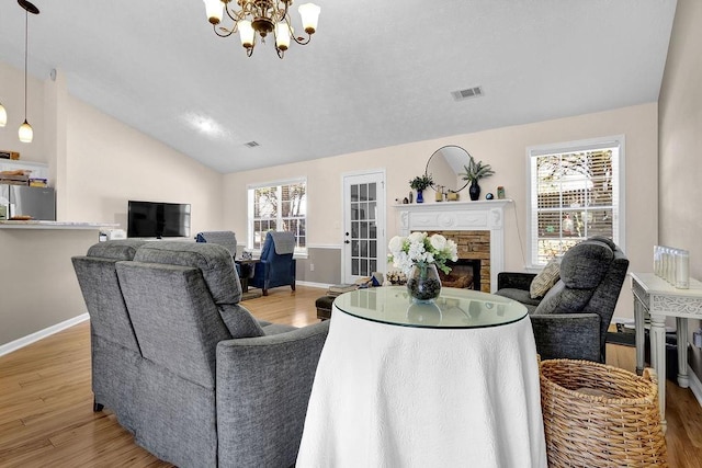 living room featuring light wood finished floors, lofted ceiling, visible vents, an inviting chandelier, and a stone fireplace