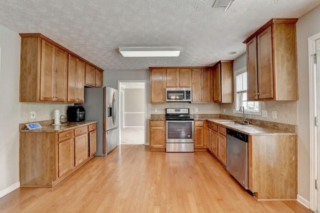 kitchen with light stone counters, a textured ceiling, stainless steel appliances, sink, and light hardwood / wood-style flooring