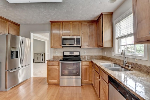 kitchen with a textured ceiling, sink, stainless steel appliances, and light hardwood / wood-style flooring