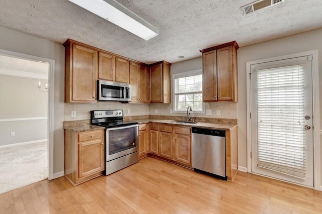 kitchen with appliances with stainless steel finishes, light wood-type flooring, light stone counters, a textured ceiling, and sink