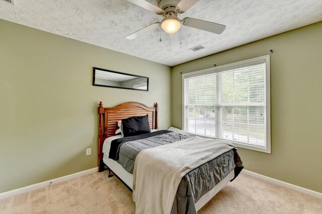 bedroom with ceiling fan, light carpet, and a textured ceiling