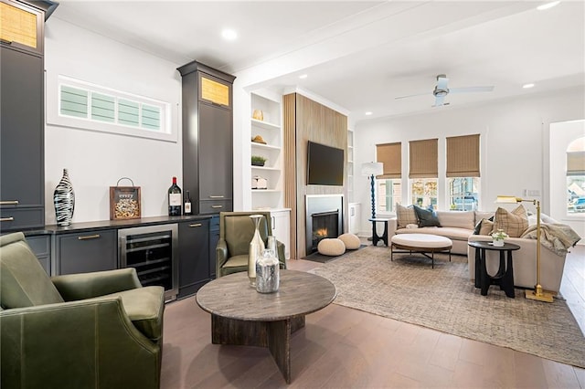 living room with wood-type flooring, beverage cooler, built in shelves, a large fireplace, and ceiling fan