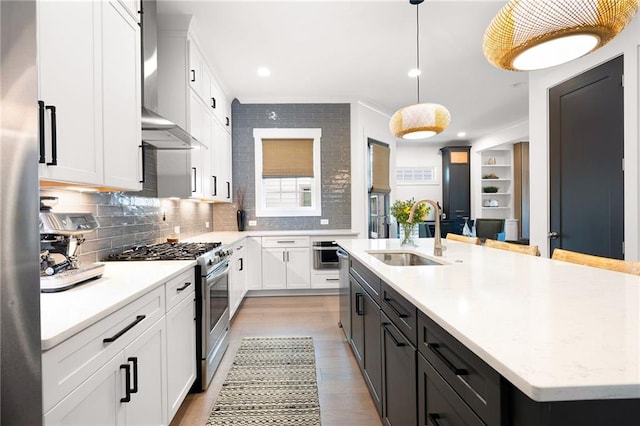 kitchen with appliances with stainless steel finishes, sink, wall chimney range hood, white cabinets, and a kitchen island with sink