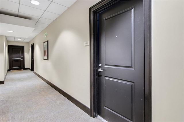 hallway featuring a drop ceiling and light colored carpet