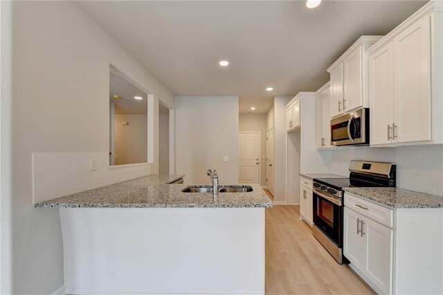 kitchen featuring light stone counters, appliances with stainless steel finishes, kitchen peninsula, and white cabinetry