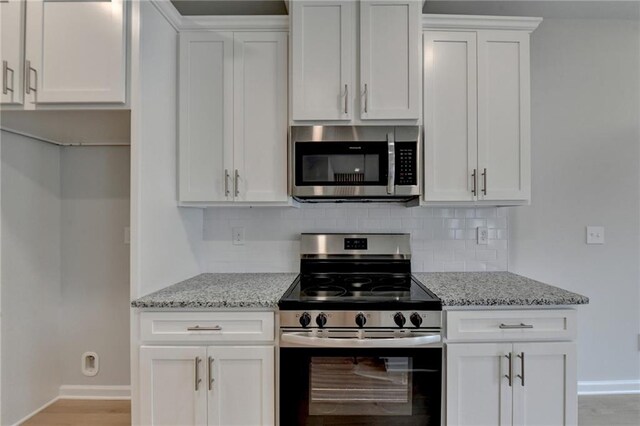 kitchen with white cabinets, stainless steel appliances, light stone counters, and backsplash